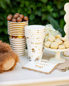 Party supplies including cups, napkins, and cookies on a table with a green background.