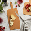 Brown cutting board with sliced cheese, knife, and cherry tomatoes on a marble surface.