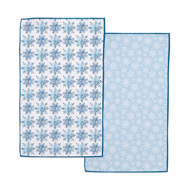 Reversible kitchen towel with snowflake patterns, shown overlapping on a white background. One side has a white base with blue snowflakes and a blue border, and the other side has a light blue base with white snowflakes and a blue border.