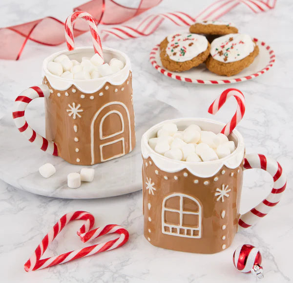 Two gingerbread-themed mugs with hot chocolate and marshmallows, surrounded by candy canes and cookies on a white surface.