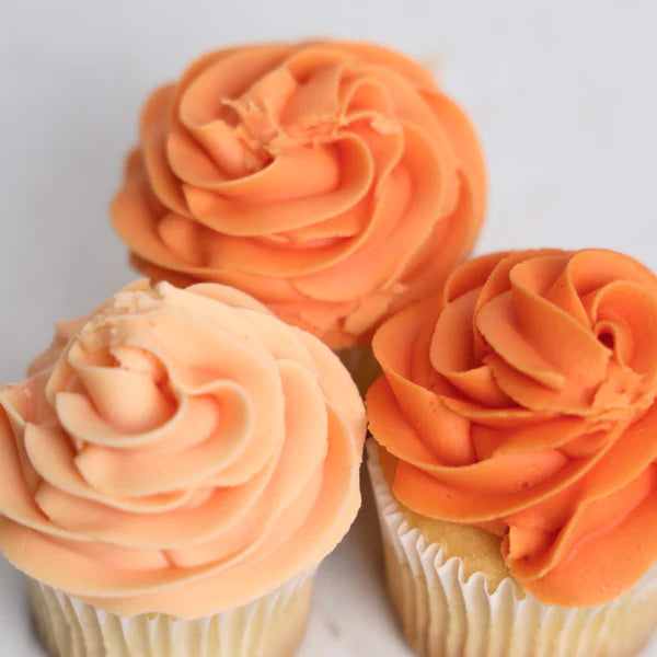 Three cupcakes with orange and peach frosting on a light background