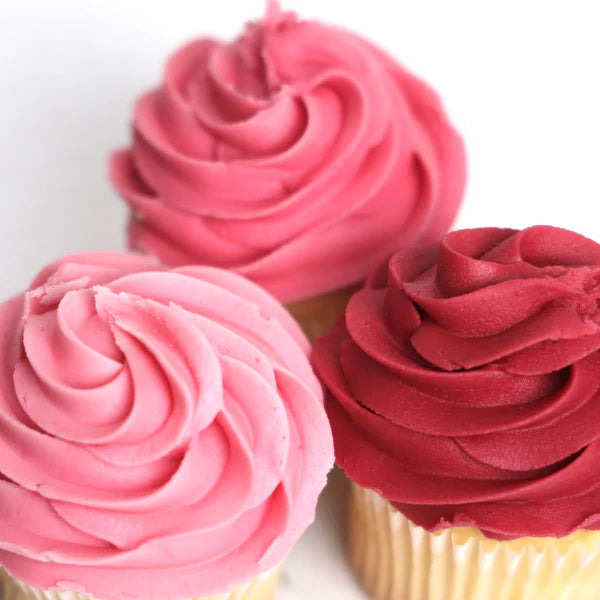 Three cupcakes with pink and red frosting on a white background