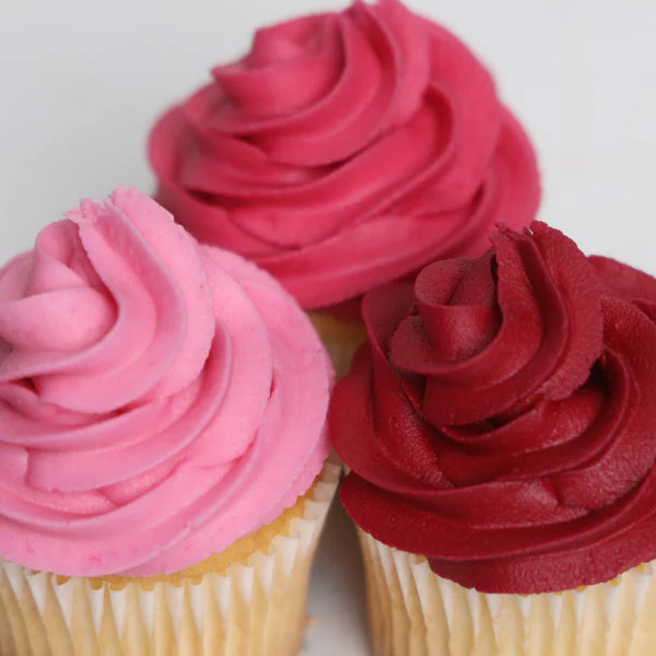 Three cupcakes with pink, red, and pink frosting on a white background