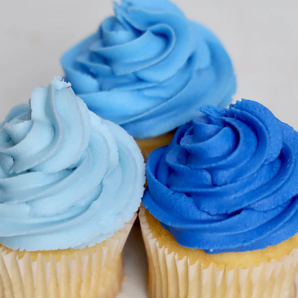 Three cupcakes with blue frosting on a light background