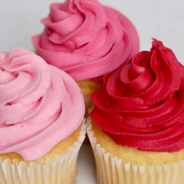Three cupcakes with pink and red frosting on a white background