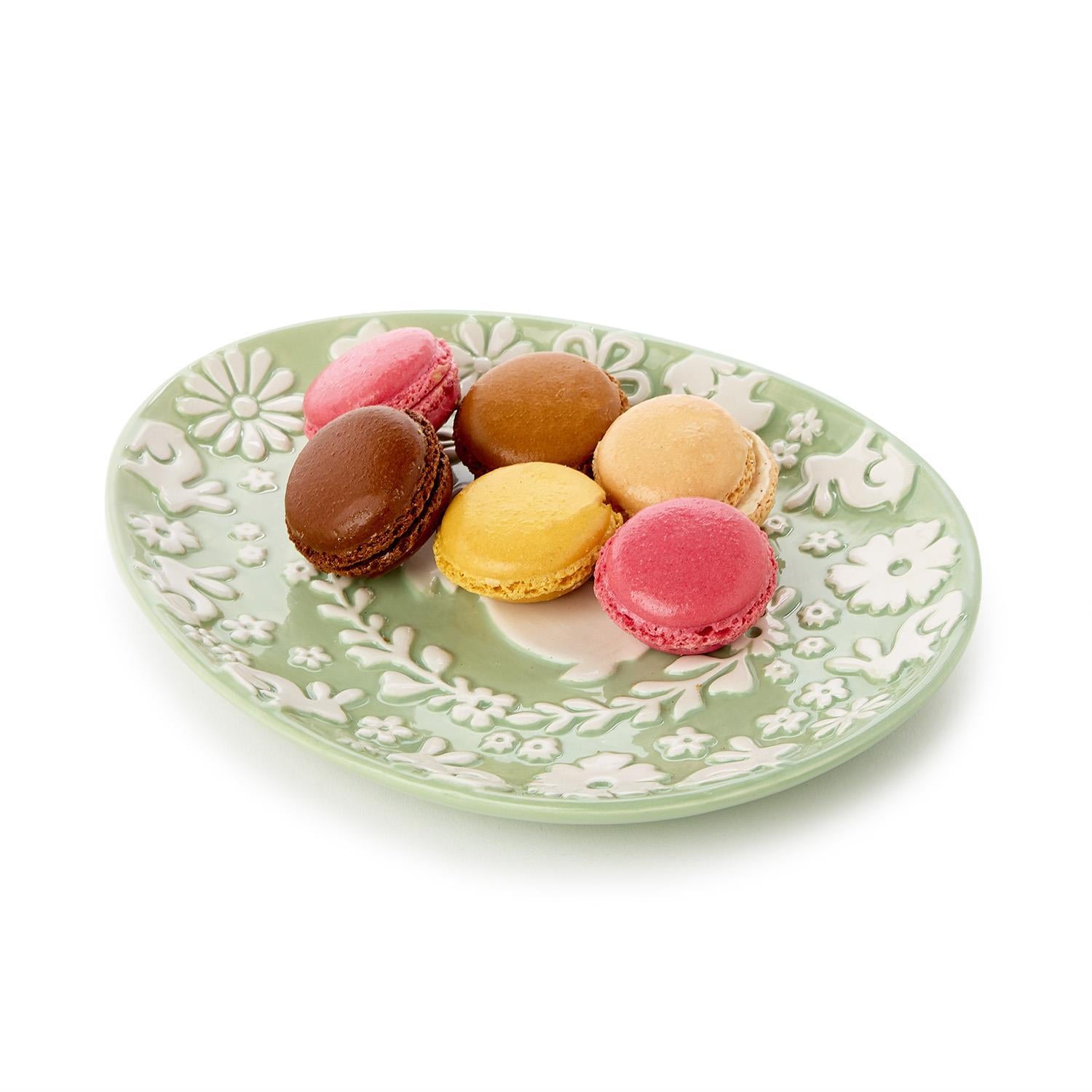 Colorful macarons on a decorative green plate with white floral patterns.