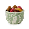 Green bowl with floral patterns and a rabbit silhouette filled with colorful macarons on a white background
