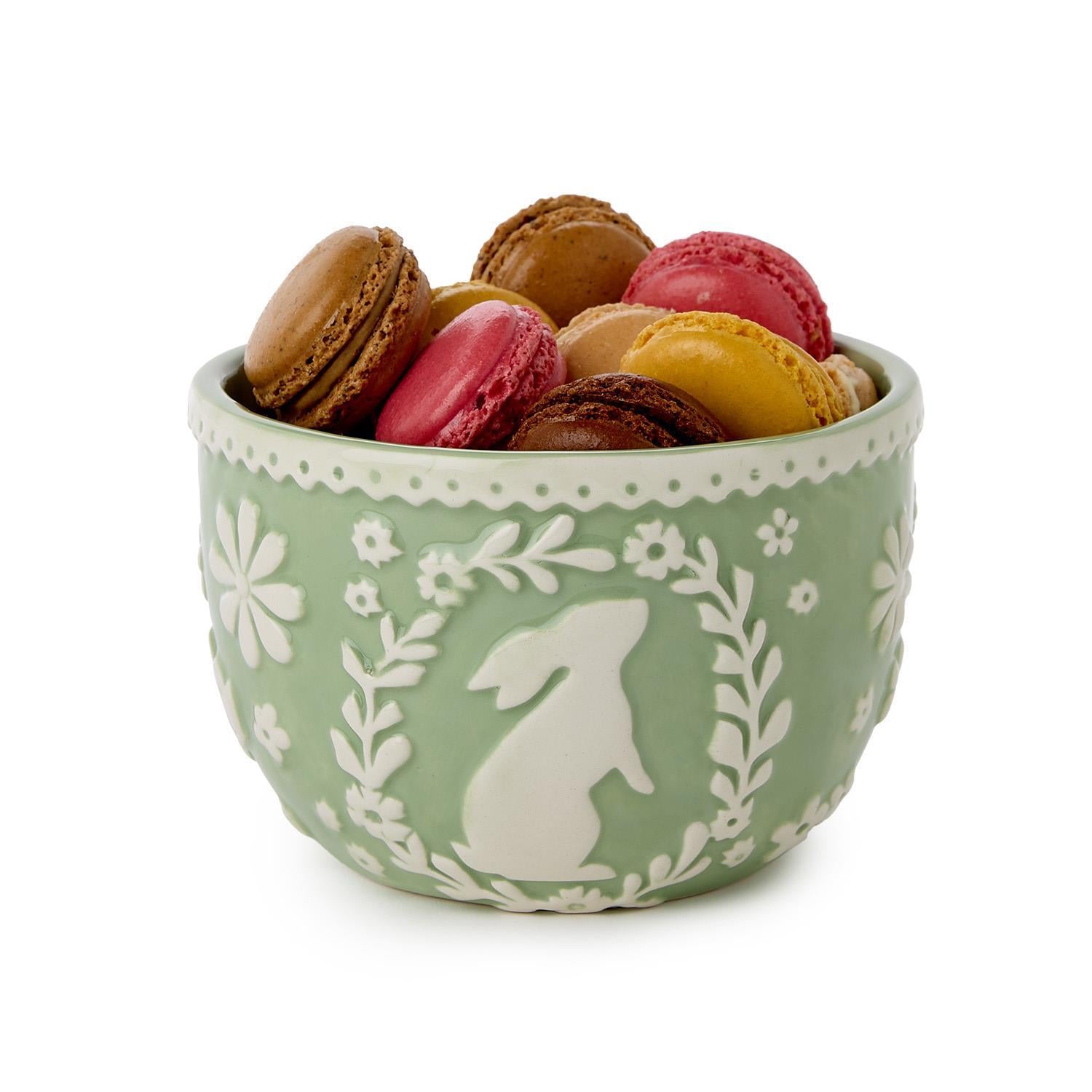 Green bowl with floral patterns and a rabbit silhouette filled with colorful macarons on a white background