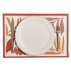 White plate with silverware on a decorative placemat with leaf pattern