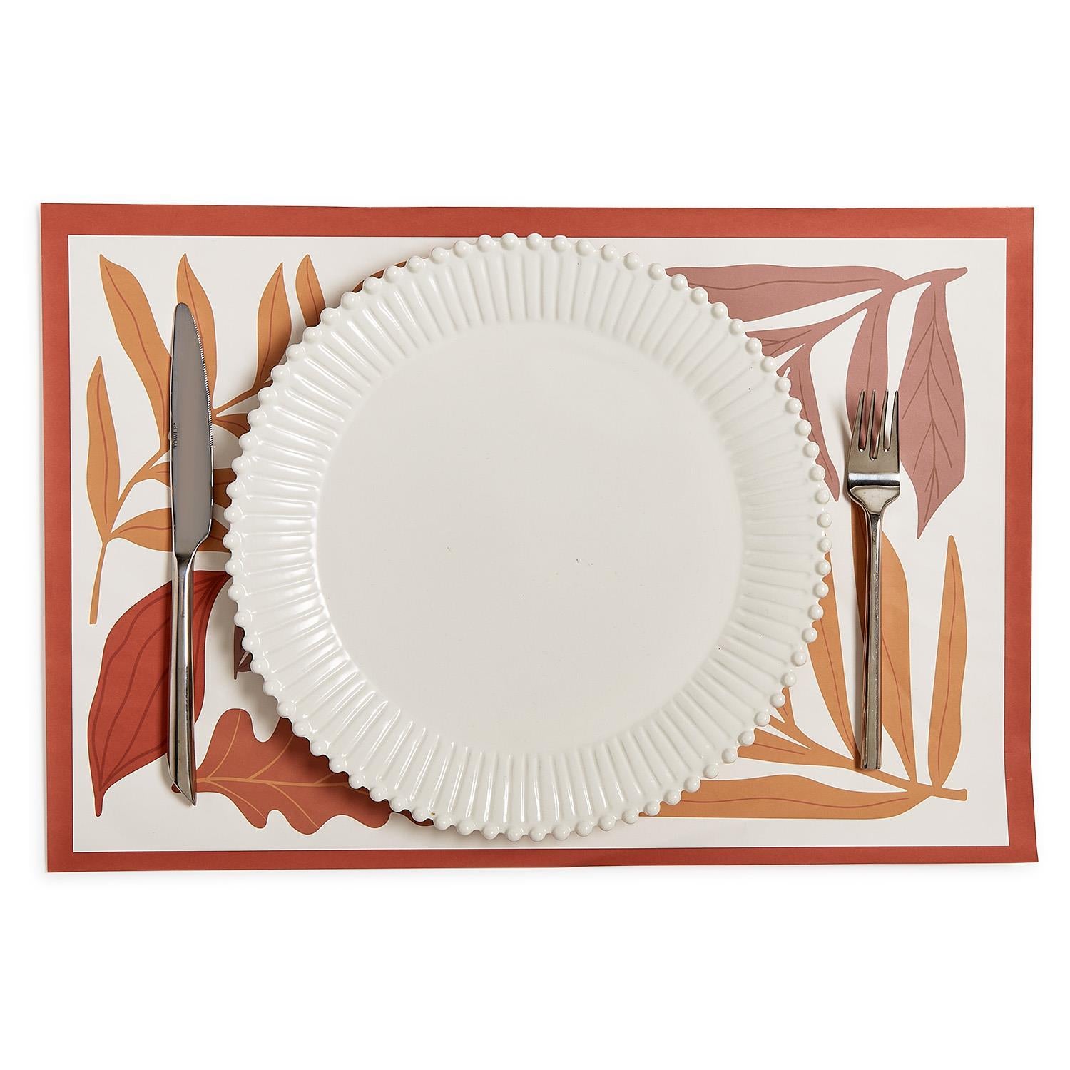 White plate with silverware on a decorative placemat with leaf pattern