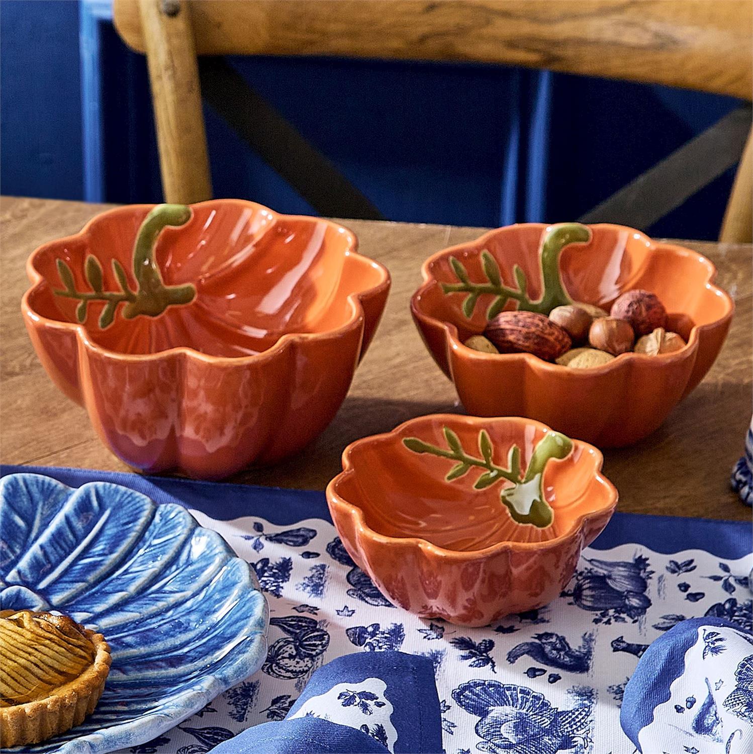 Three pumpkin-shaped bowls with leaf designs on a table with blue accents.
