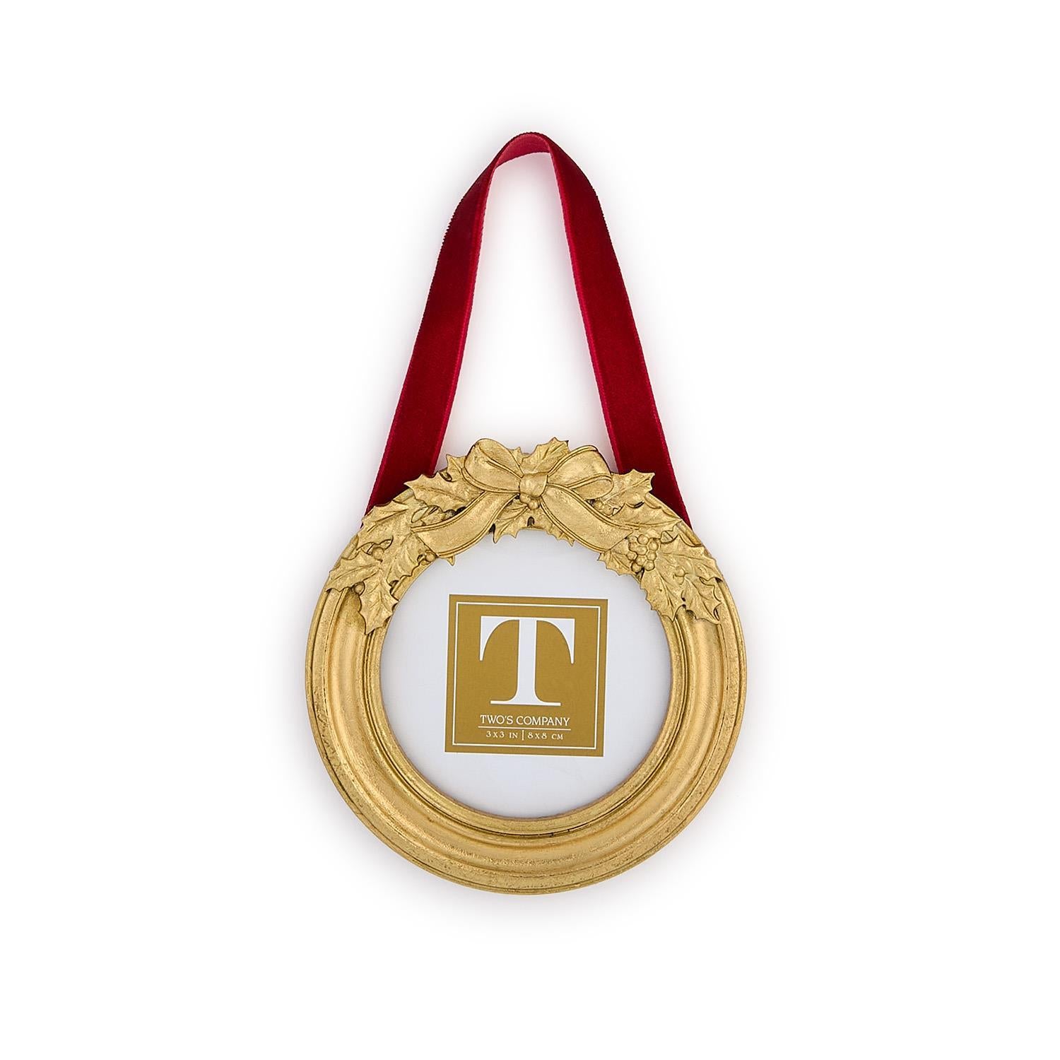 Decorative gold ornament with a red ribbon and holly leaf embellishments on a white background