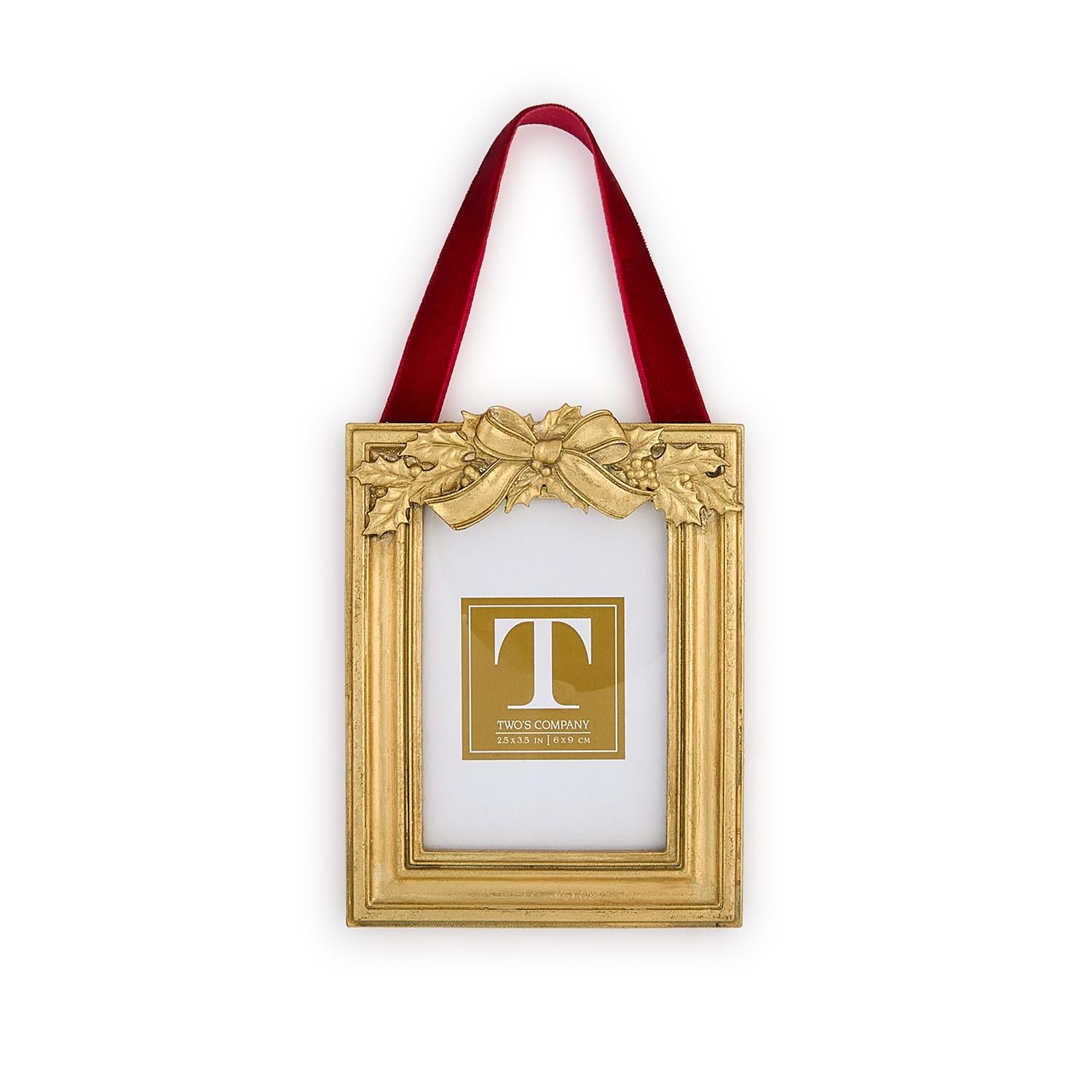 Gold decorative frame with a red ribbon and holly leaf embellishments on a white background