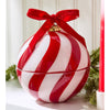 A red and white striped ornament-shaped candle with red ribbon on a white background with greenery in the backgound.