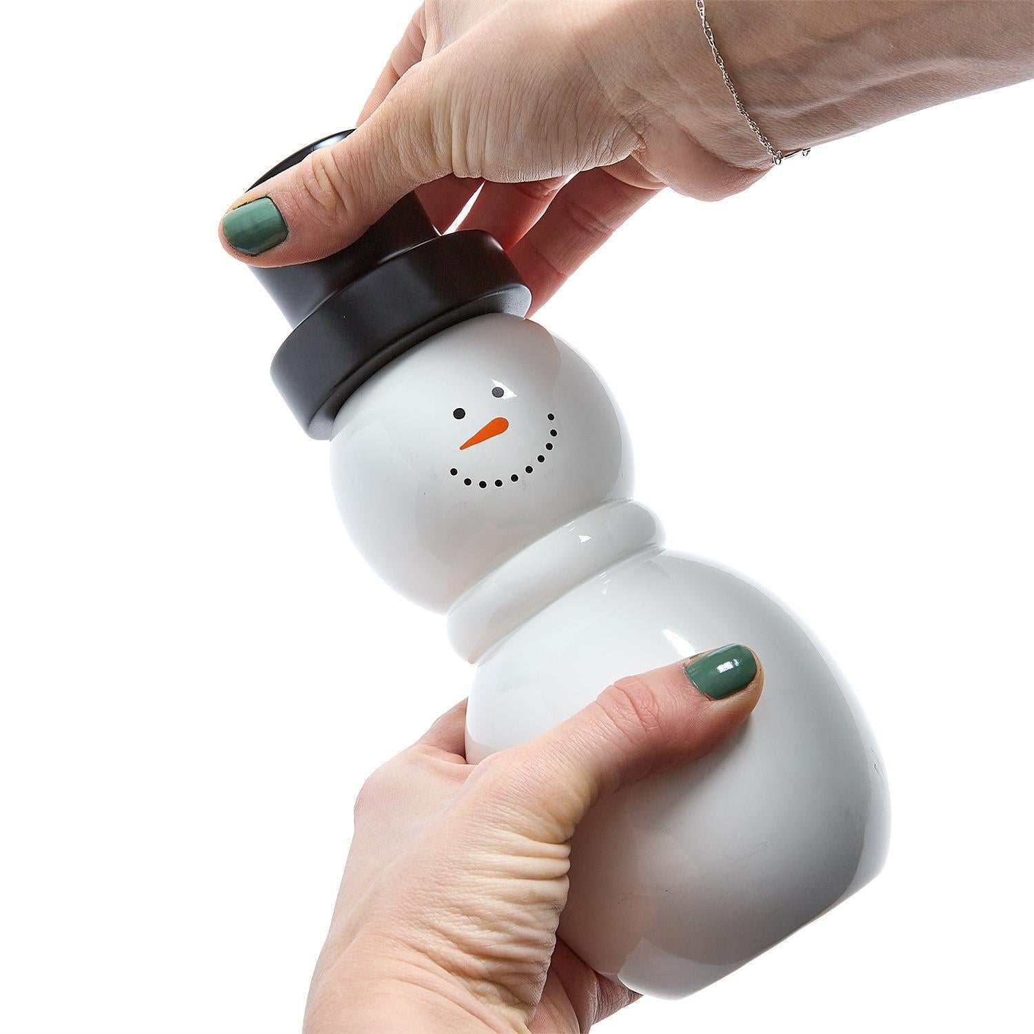 Snowman-shaped pepper grinder held by a hand on a white background