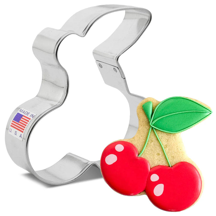 Metallic cherry-shaped cookie cutter with a cookie shaped like a cherry on a white background