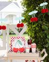 Outdoor setting with cherry-themed decor including a plate, cups, and decorative banner.