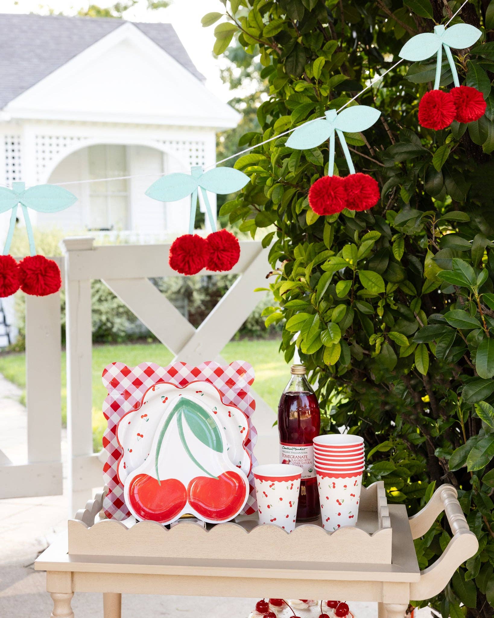 Outdoor setting with cherry-themed decor including a plate, cups, and decorative banner.