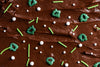 Chocolate frosted cake with green and white sprinkles on a brown background