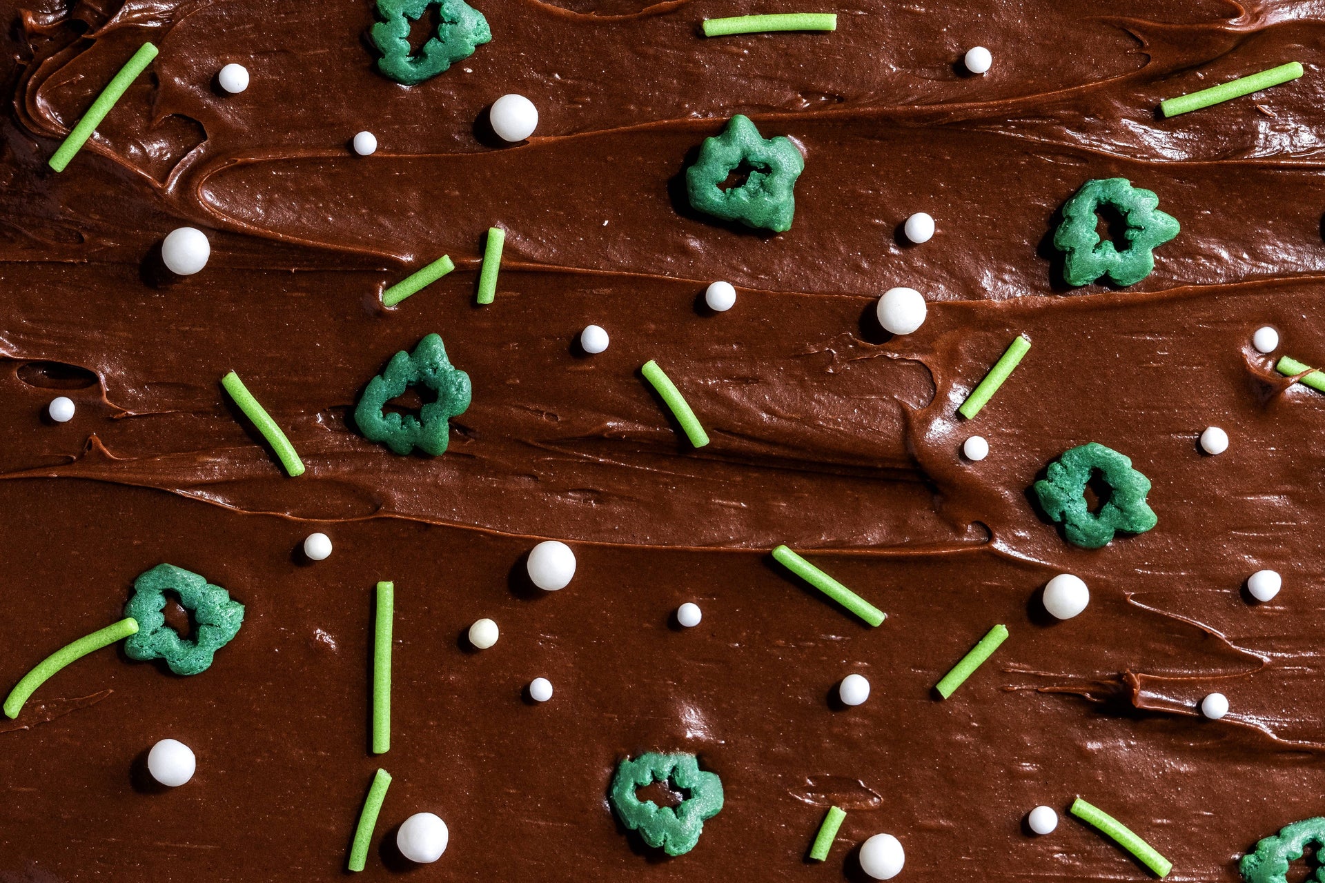 Chocolate frosted cake with green and white sprinkles on a brown background