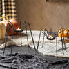 Spider-shaped candle holders on a Halloween-themed table with pumpkins and spider webs.