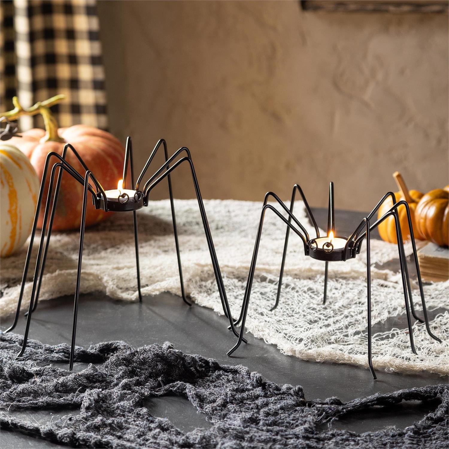 Spider-shaped candle holders on a Halloween-themed table with pumpkins and spider webs.