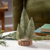 Three decorative Christmas trees on a wooden base with snow and greenery.