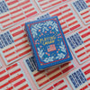 Playing card box with floral design and American flag on a pink background with red and blue cards.