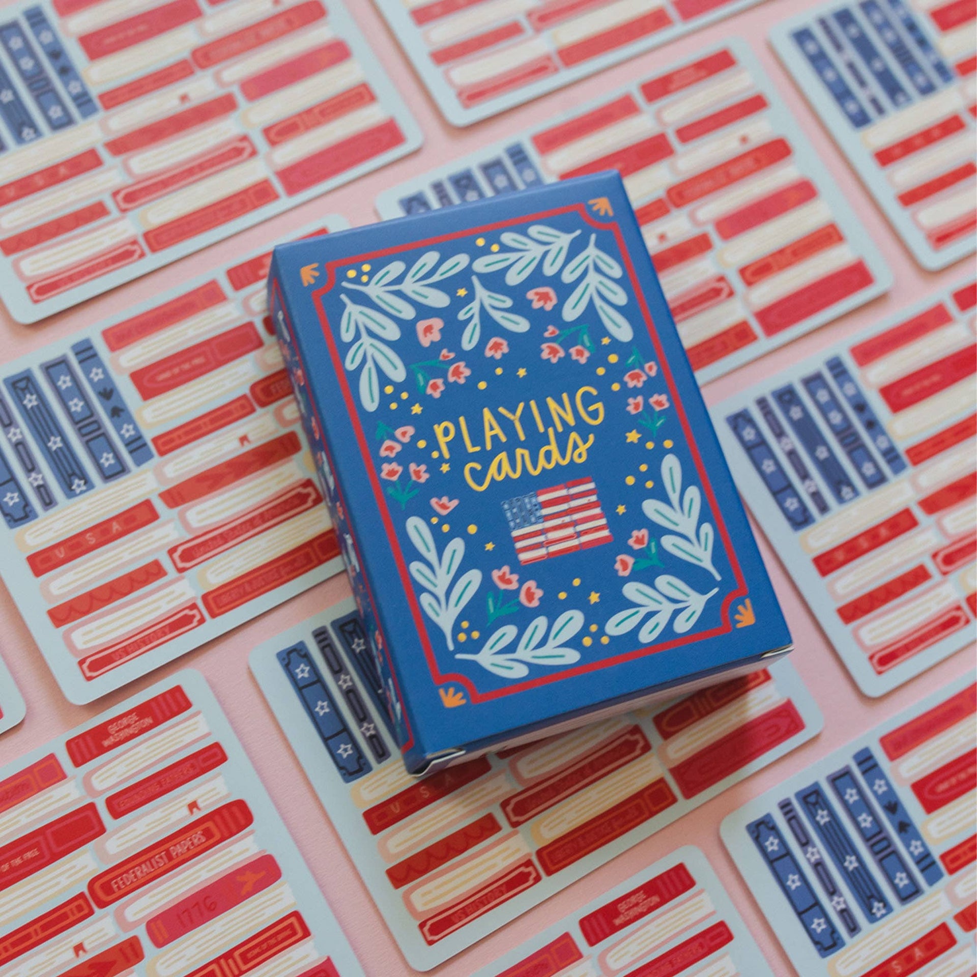 Playing card box with floral design and American flag on a pink background with red and blue cards.