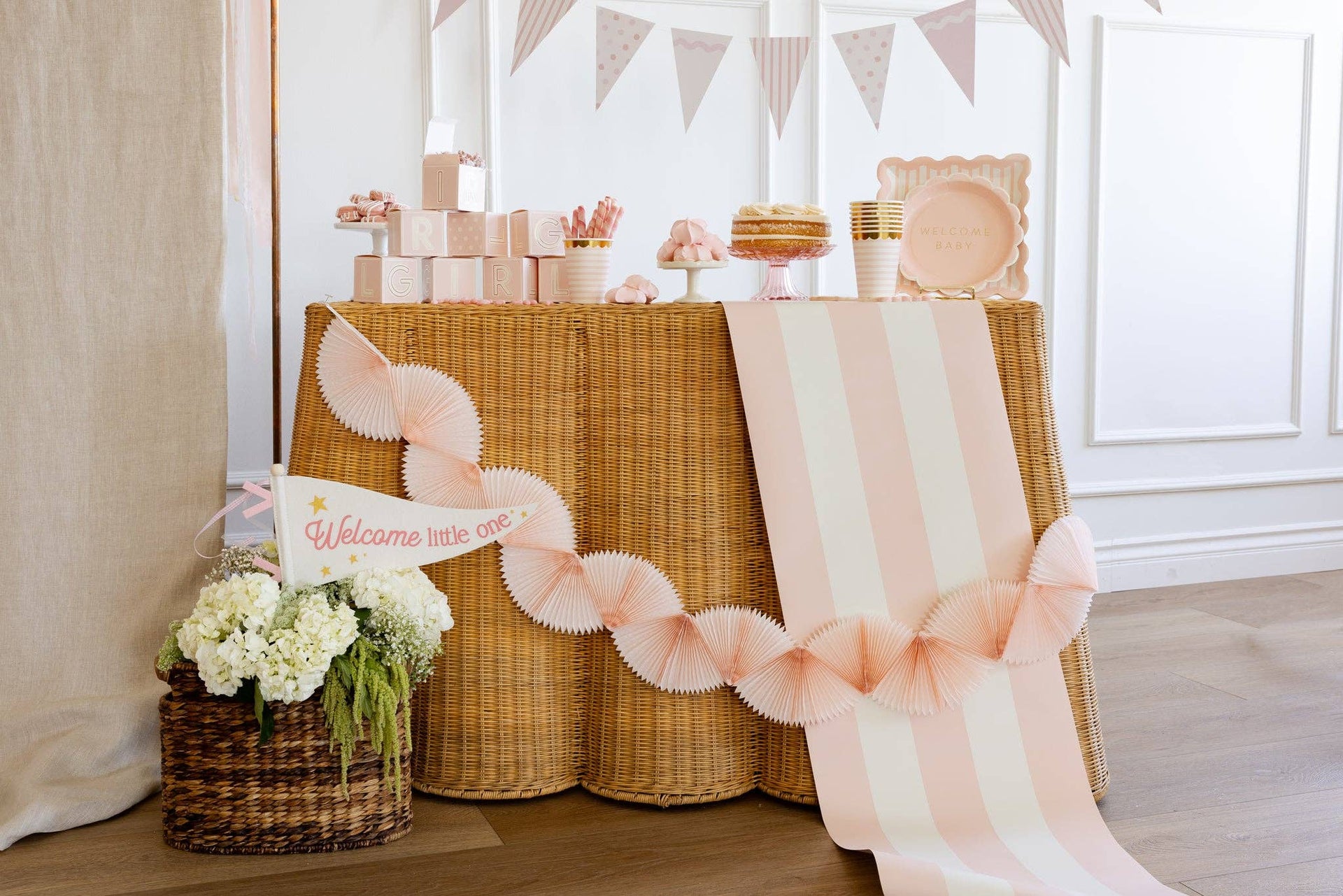 Decorated table with pink ribbons, flowers, and a 'Welcome little one' sign in a baby shower setting.