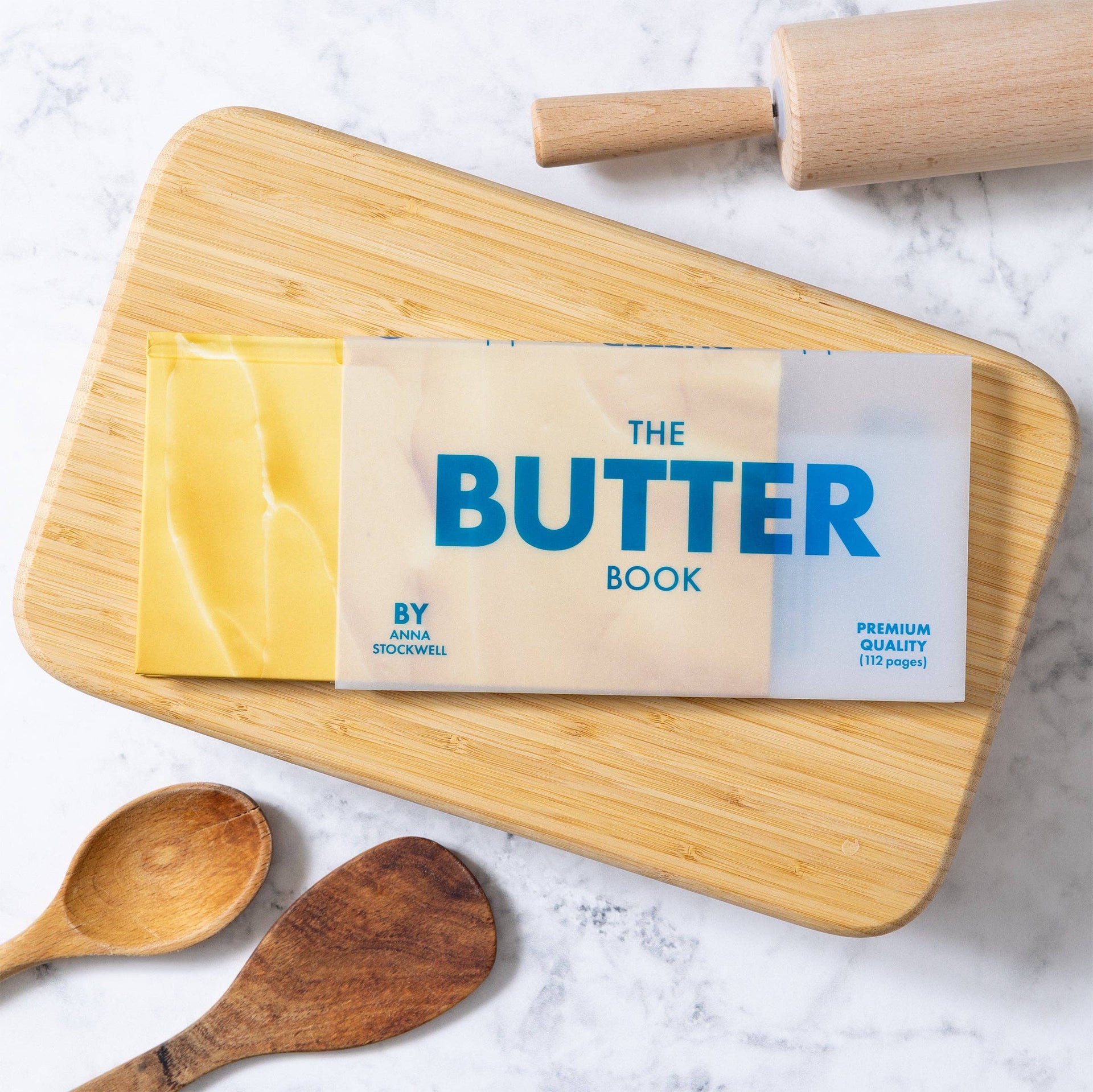 Book titled The Butter book on a wooden cutting board with a rolling pin and wooden spoons.