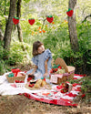 Child at a picnic setup in a forest with a basket and food and strawberry themed products.
