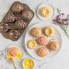 Decorative rose-shaped baking mold with baked goods on a marble surface.