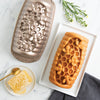 Honeycomb-shaped baked good next to a honeycomb mold and plate of honey on a marble surface.