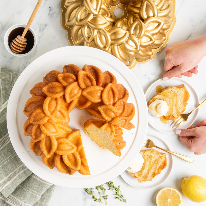 Decorative bundt cake on a white plate with a gold bundt cake pan in the background.