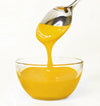 Yellow frosting being poured from a spoon into a glass bowl on a white background