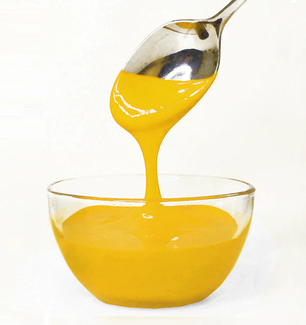 Yellow frosting being poured from a spoon into a glass bowl on a white background