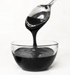 Spoon pouring black frosting into a clear glass bowl on a white background