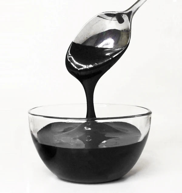 Spoon pouring black frosting into a clear glass bowl on a white background