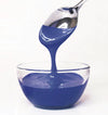 Spoon pouring blue frosting into a glass bowl on a white background