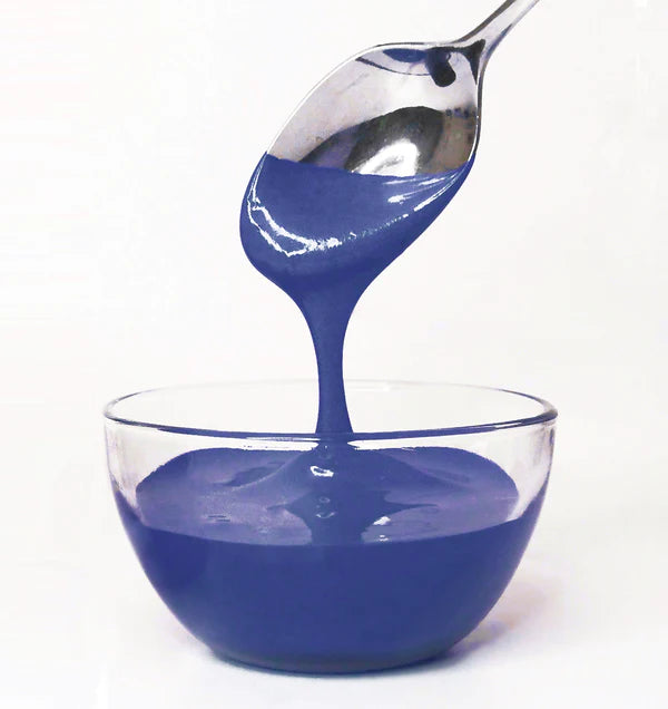 Spoon pouring blue frosting into a glass bowl on a white background