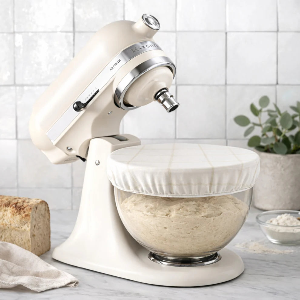 White KitchenAid stand mixer with dough in a bowl covered by a beeswax bowl cover on a kitchen counter. 