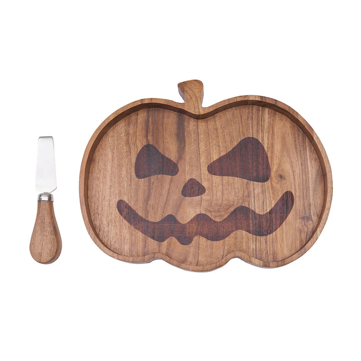 Wooden serving board shaped like a pumpkin with a carved face and a knife on a white background