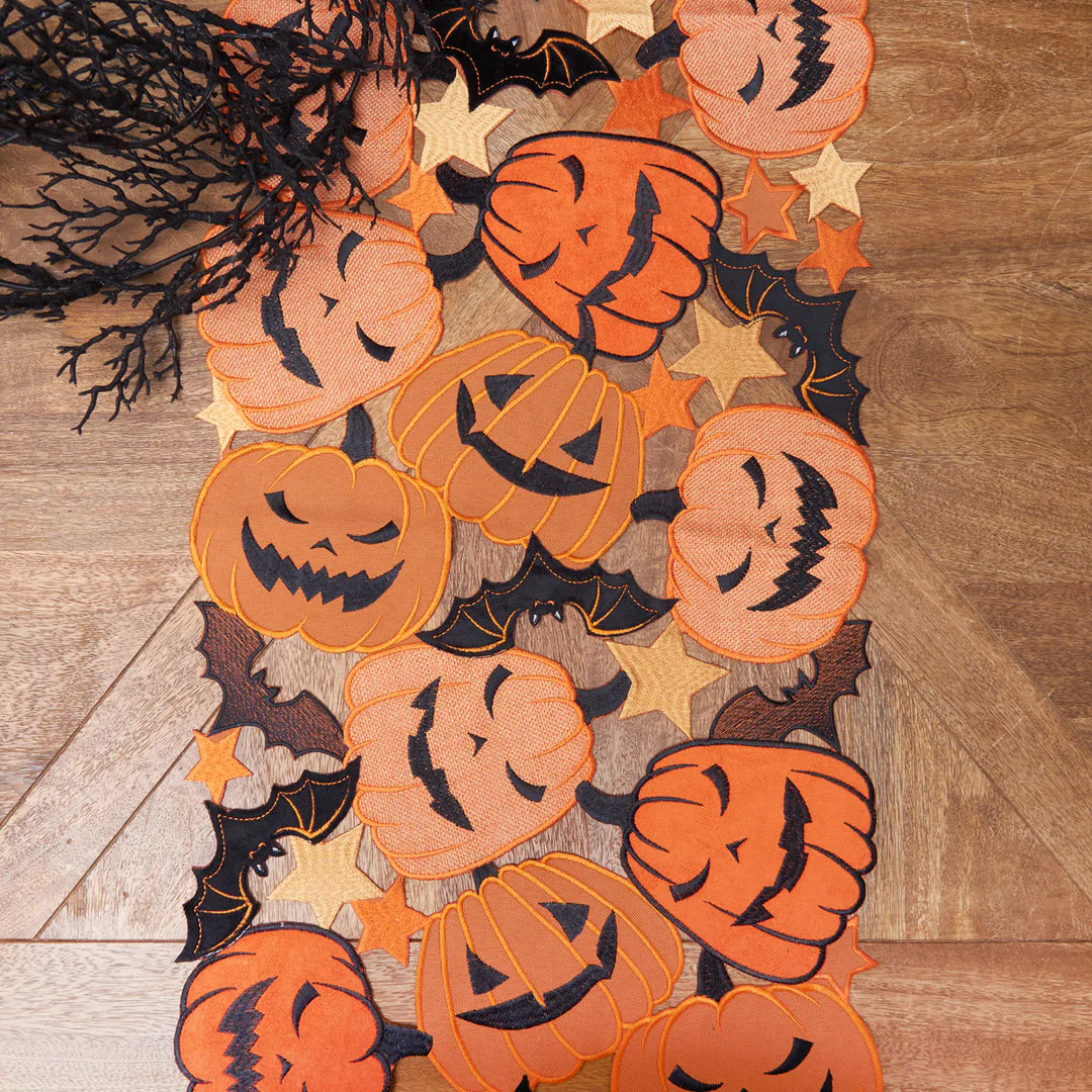 Halloween-themed decorative table runner with pumpkins and bats on a wooden table.
