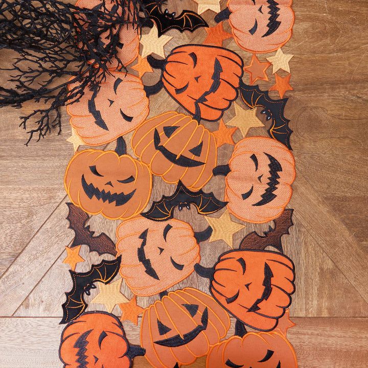 Halloween-themed decorative table runner with pumpkins and bats on a wooden table.