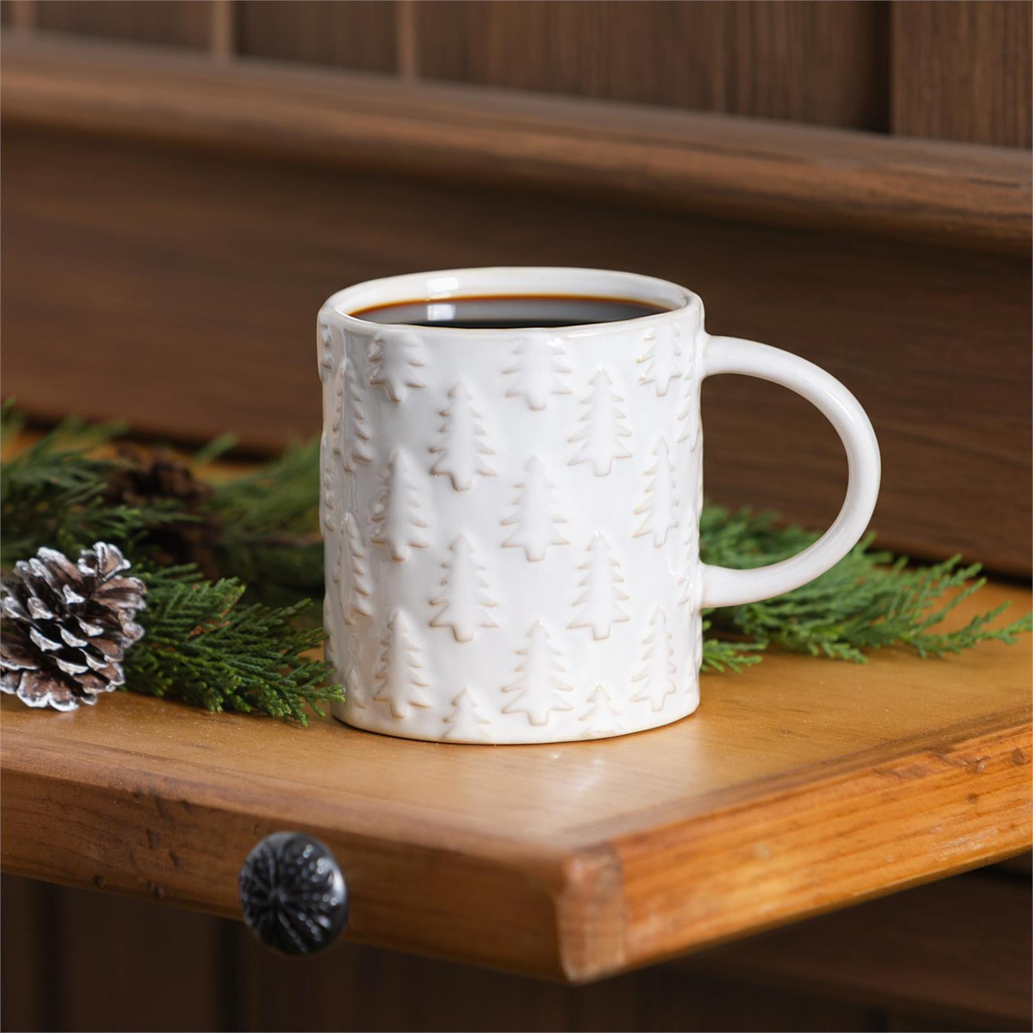 White textured mug with coffee on a wooden shelf with greenery and pine cones.