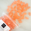 Orange gummy bears spilling out of a clear container with a white lid on a light background