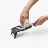 Person using a mandoline to slice a potato on a white background
