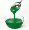 Green frosting being poured from a spoon into a glass bowl on a white background