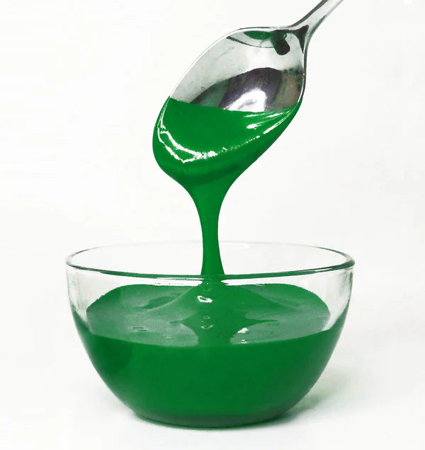 Green frosting being poured from a spoon into a glass bowl on a white background